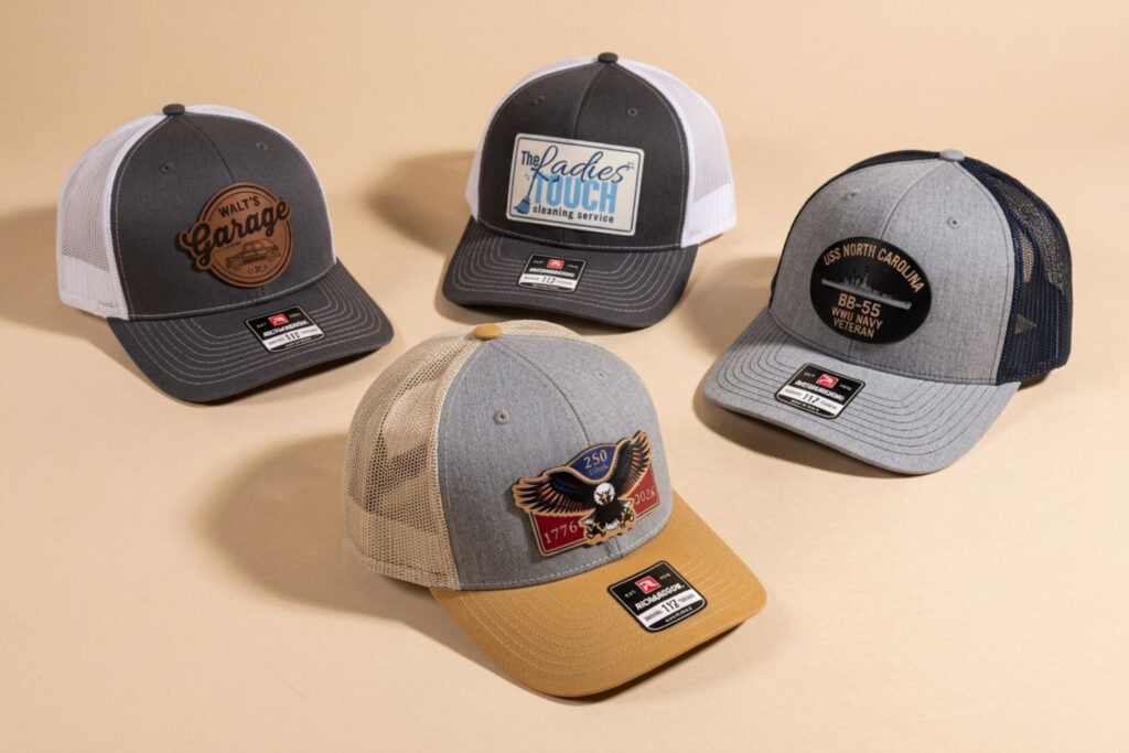 Four different trucker hats with mesh backs and various embroidered patches are displayed on a beige surface.