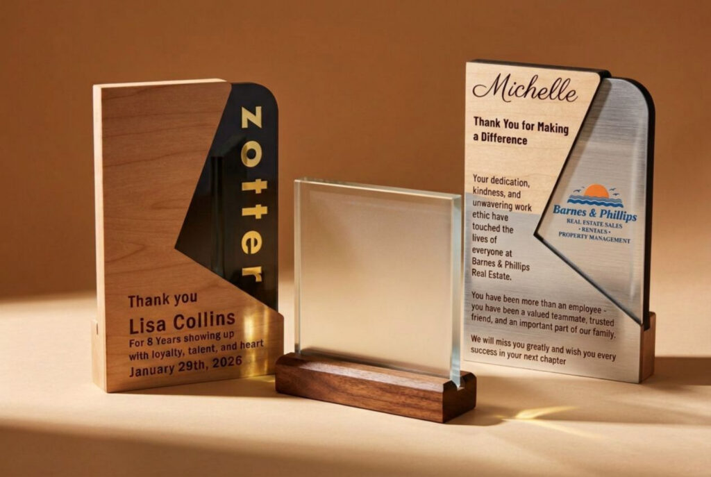 Three award plaques are displayed on a brown background; two are engraved with personalized messages, and one is a blank frosted glass plaque on a wooden stand.