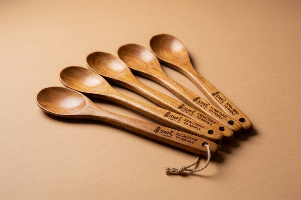 Five wooden cooking spoons with engraved handles are arranged in a fanned-out pattern on a light brown background.